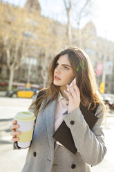 Spanien, Barcelona, junge Geschäftsfrau mit Kaffee zum Mitnehmen beim Telefonieren - VABF01563