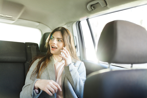 Porträt einer jungen Geschäftsfrau, die auf der Rückbank eines Autos sitzt und telefoniert, lizenzfreies Stockfoto