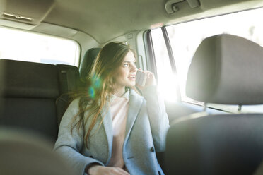 Junge Geschäftsfrau am Telefon auf der Rückbank eines Autos sitzend und aus dem Fenster schauend - VABF01570
