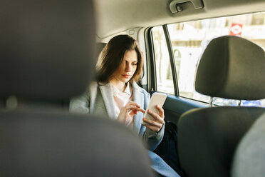 Junge Geschäftsfrau sitzt auf der Rückbank eines Autos und benutzt ein Mobiltelefon - VABF01573