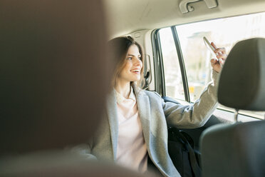 Lächelnde junge Geschäftsfrau sitzt auf dem Rücksitz eines Autos und macht ein Selfie mit ihrem Handy - VABF01574