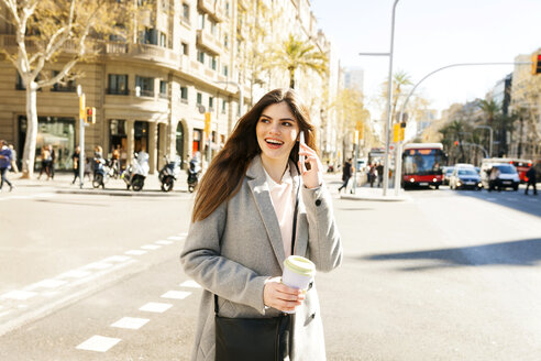 Spain, Barcelona, portrait of smiling young woman on the phone standing at roadside - VABF01582