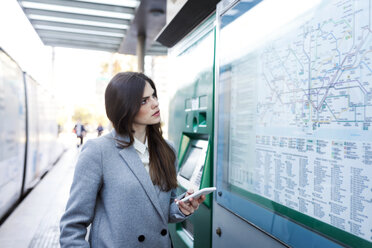 Spain, Barcelona, young woman with smartphone looking at map at station - VABF01586