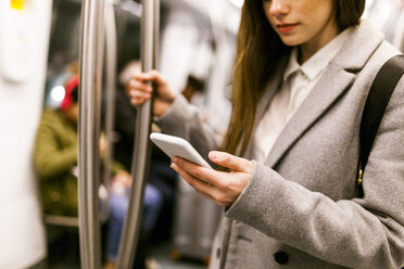 Businesswoman using cell phone in underground train, partial view - VABF01603