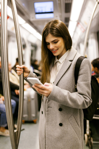 Spanien, Barcelona, junge Geschäftsfrau benutzt Handy in der U-Bahn, lizenzfreies Stockfoto
