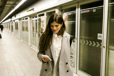 Young woman using cell phone and earphones in a passageway - VABF01608