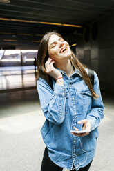 Portrait of happy young woman listening music with cell phone and earphones - VABF01611