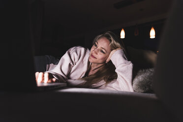 Smiling woman lying on couch at home using laptop - UUF13481