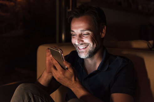 Portrait of happy mature man using cell phone at home - UUF13494