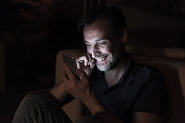 Porträt eines glücklichen reifen Mannes, der zu Hause ein Mobiltelefon benutzt - UUF13495