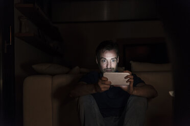 Man sitting in the dark at home starring at smartphone - UUF13497