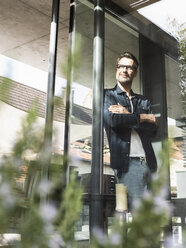 Content mature man standing in front of terrace door of his house - UUF13507