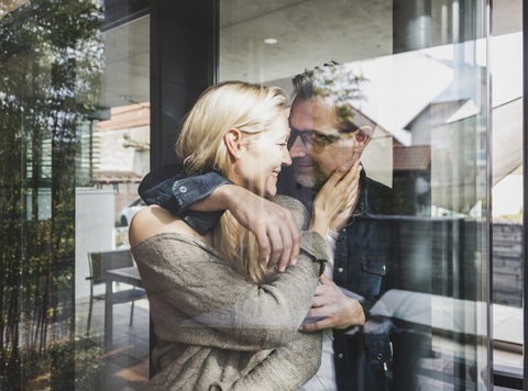 Happy mature couple behind windowpane at home stock photo