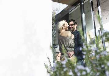 Glückliches reifes Paar steht auf der Terrasse seines Hauses - UUF13512
