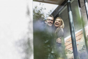 Glückliches reifes Paar steht auf der Terrasse seines Hauses - UUF13515