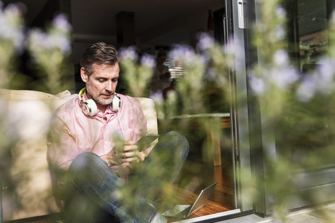 Mature man sitting at open terrace door using smartphone stock photo
