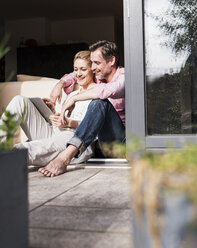 Älteres Paar entspannt sich zusammen bei offener Terrassentür und benutzt ein Tablet - UUF13548