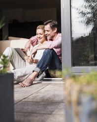 Mature couple relaxing together at open terrace door using tablet - UUF13548