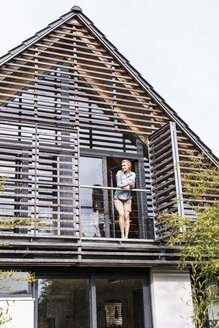 Frau steht auf dem Balkon ihres Hauses und schaut in die Ferne - UUF13549