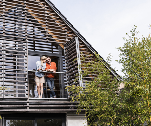 Glückliches reifes Paar steht auf dem Balkon seines Hauses, lizenzfreies Stockfoto