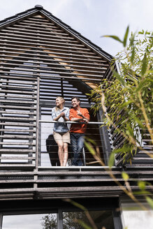 Lächelndes reifes Paar steht auf dem Balkon seines Hauses - UUF13561