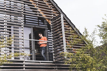 Man standing on balcony of his house looking at smartphone - UUF13562