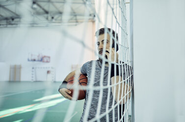 Man with basketball using smartphone behind net, indoor - ZEDF01382