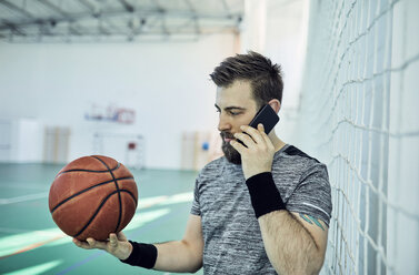 Man with basketball using smartphone, indoor - ZEDF01383