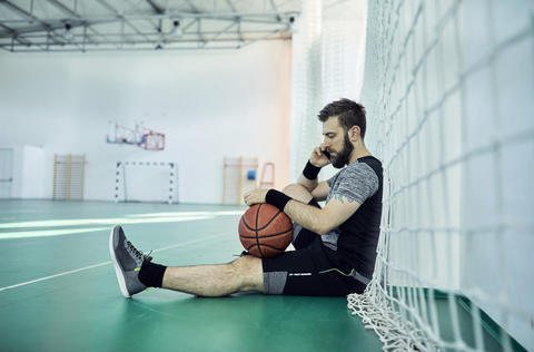 Man with basketball using smartphone, indoor stock photo