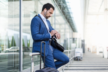 Businessman at airport, looking on watch - DIGF04189