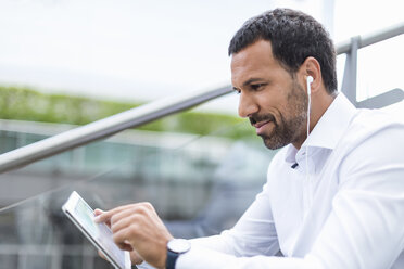 Businessman using tablet, earphones - DIGF04205