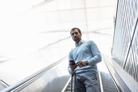 Geschäftsmann mit Smartphone auf Rolltreppe, lizenzfreies Stockfoto