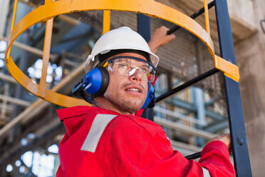 Arbeiter, der in einer Ölraffinerie auf eine Leiter steigt - CUF01227