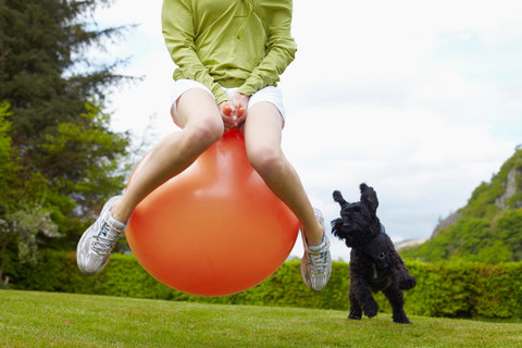 Woman on bouncy ball playing with dog stock photo