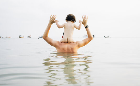 Rückenansicht eines Vaters, der seine kleine Tochter auf den Schultern ins Meer trägt - GEMF01927