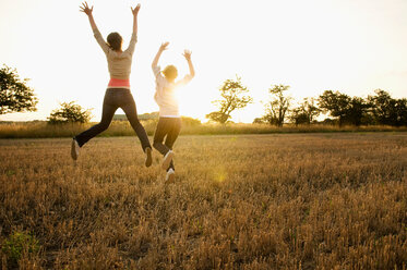 Two young girls leaping in a corn field - CUF01837