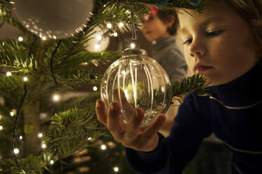 Boy decorating Christmas tree with baubles at home - ISF00358