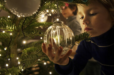 Junge schmückt Weihnachtsbaum mit Kugeln zu Hause - ISF00358