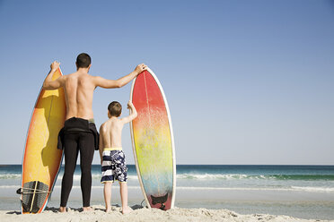 Father and son with surfboards gazing out to sea - ISF00522