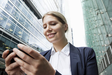 Businesswoman using smartphone amongst office buildings - ISF00524