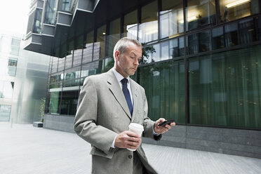 Geschäftsmann beim Spaziergang mit Smartphone und Kaffee - ISF00526