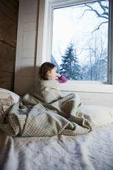 Junges Mädchen sitzt auf dem Bett und schaut durch das Fenster - ISF00545