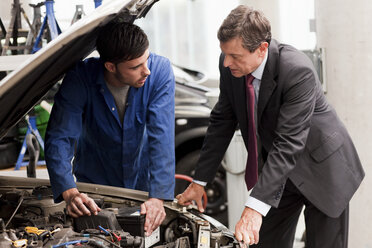 Businessman looking at car engine with mechanic - ISF00584