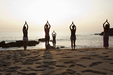 Frauen üben Yoga am Strand bei Sonnenuntergang - ISF00604
