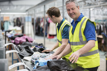 Two men sorting clothes on conveyor belt in warehouse - ISF00644