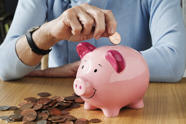 Senior woman inserting coins into piggybank - ISF00690