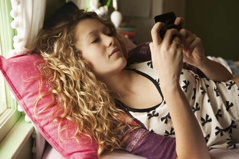 Teenager-Mädchen auf dem Bett liegend mit Smartphone - ISF00725