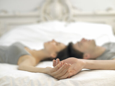 Junges Paar auf dem Bett liegend, Hände haltend - ISF00773