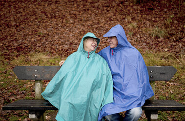 Älteres Paar auf einer Parkbank sitzend und wasserdicht gekleidet - ISF00792