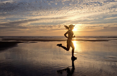 Woman running on beach at sunrise - ISF00909